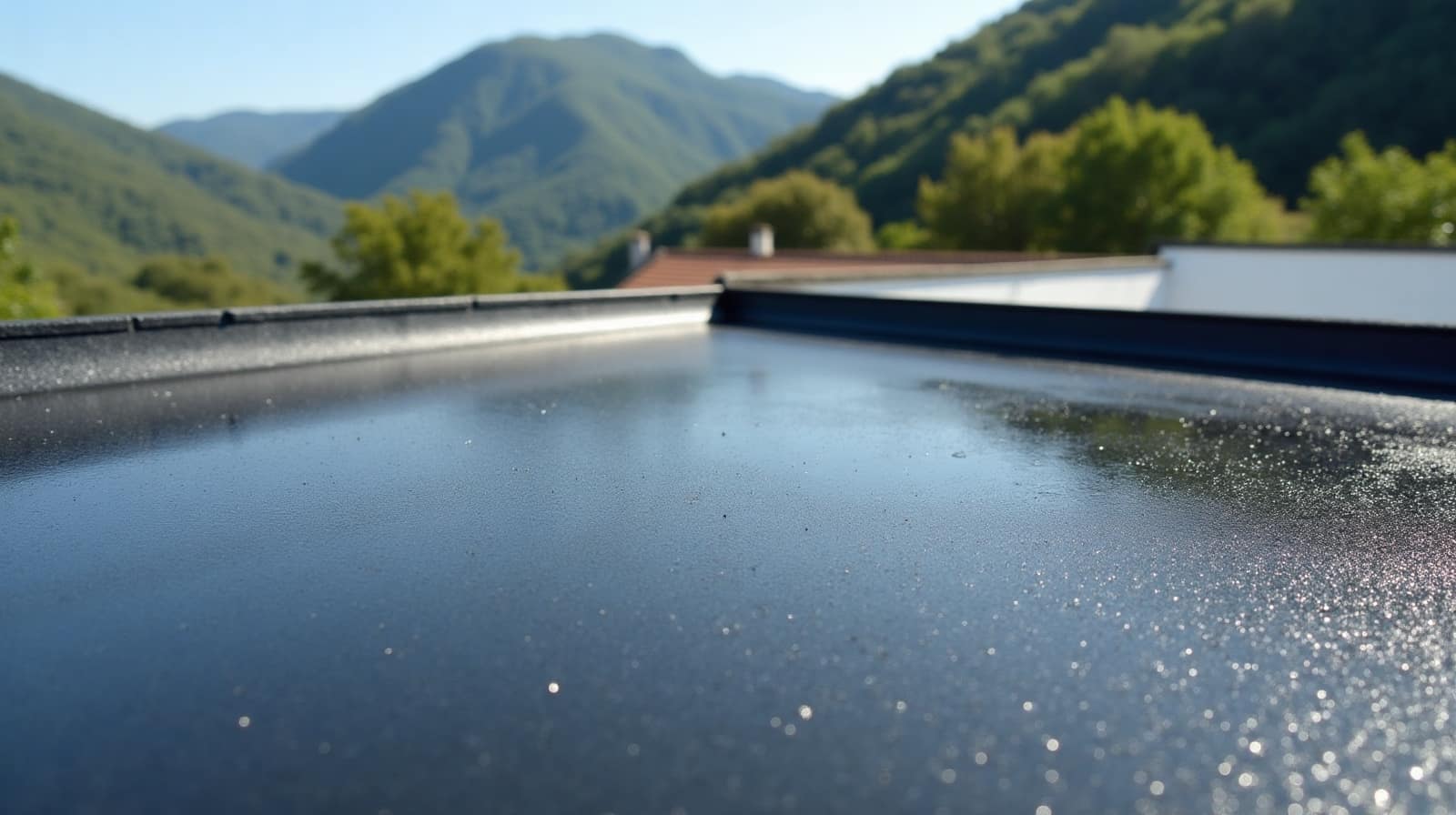 Toiture-terrasse sombre encore humide après une averse, acrotère blanc et versants boisés proches